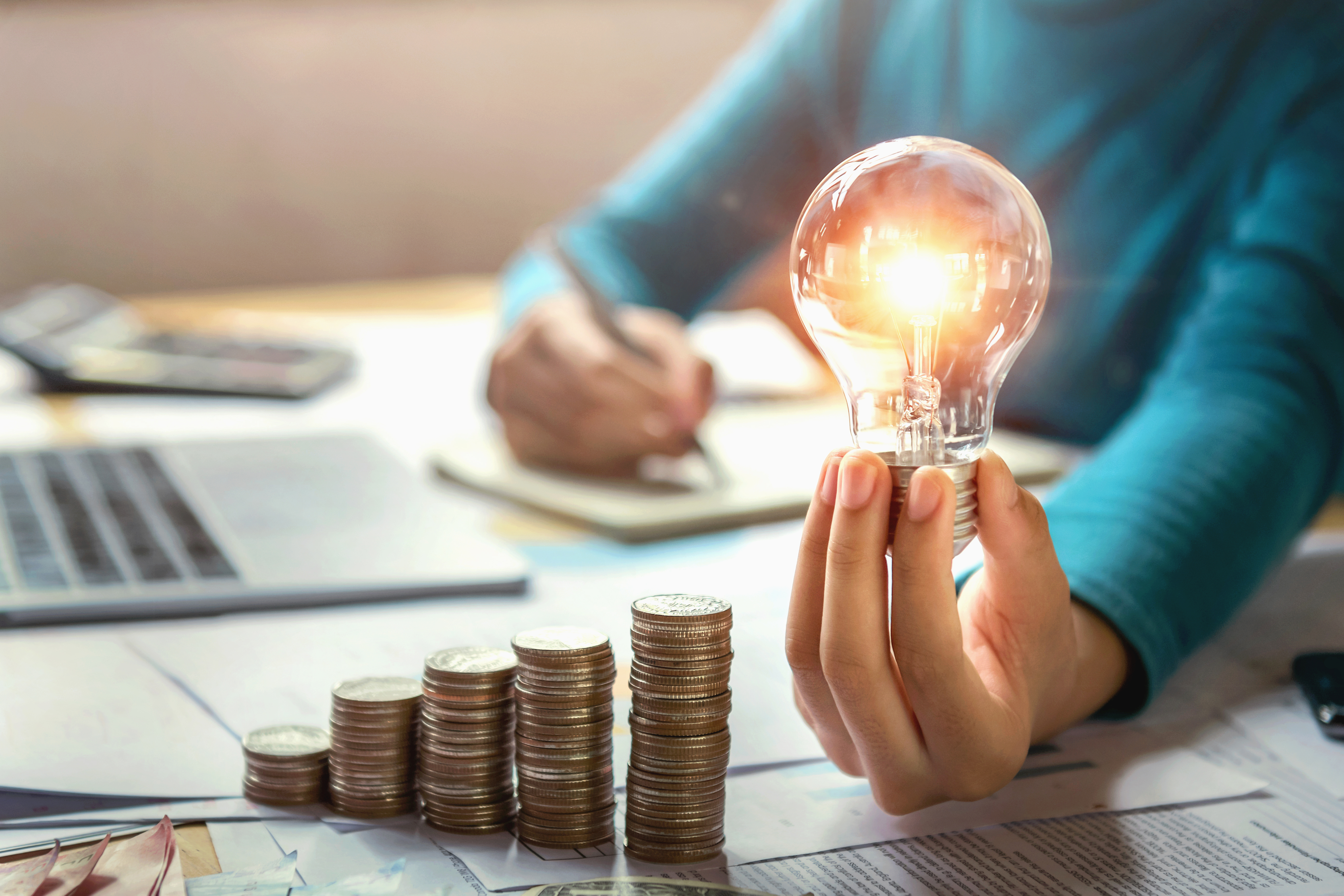 business-woman-hand-holding-lightbulb-with-coins-stack-desk-concept-saving-energy-money.jpg